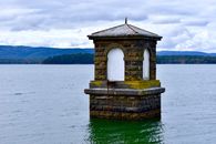 A solitary tower in Yan Yean Reservoir, Victoria, surrounded by tranquil waters and rolling hills under a cloudy sky.