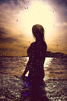 日落时分，水中一名女子的轮廓迷人，水滴营造出戏剧性的效果
