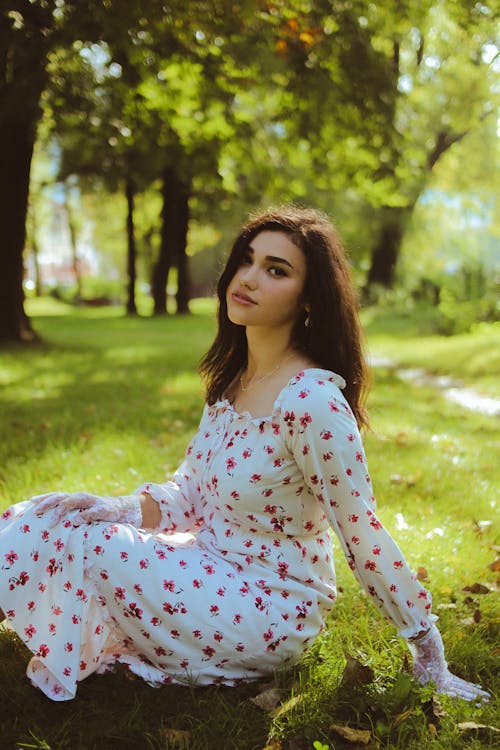 Portrait of a Pretty Brunette Wearing a Floral Dress Sitting on the Grass