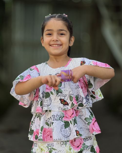 Free Joyful child playing outside, wearing a floral blouse and bracelets with a cheerful smile. Stock Photo