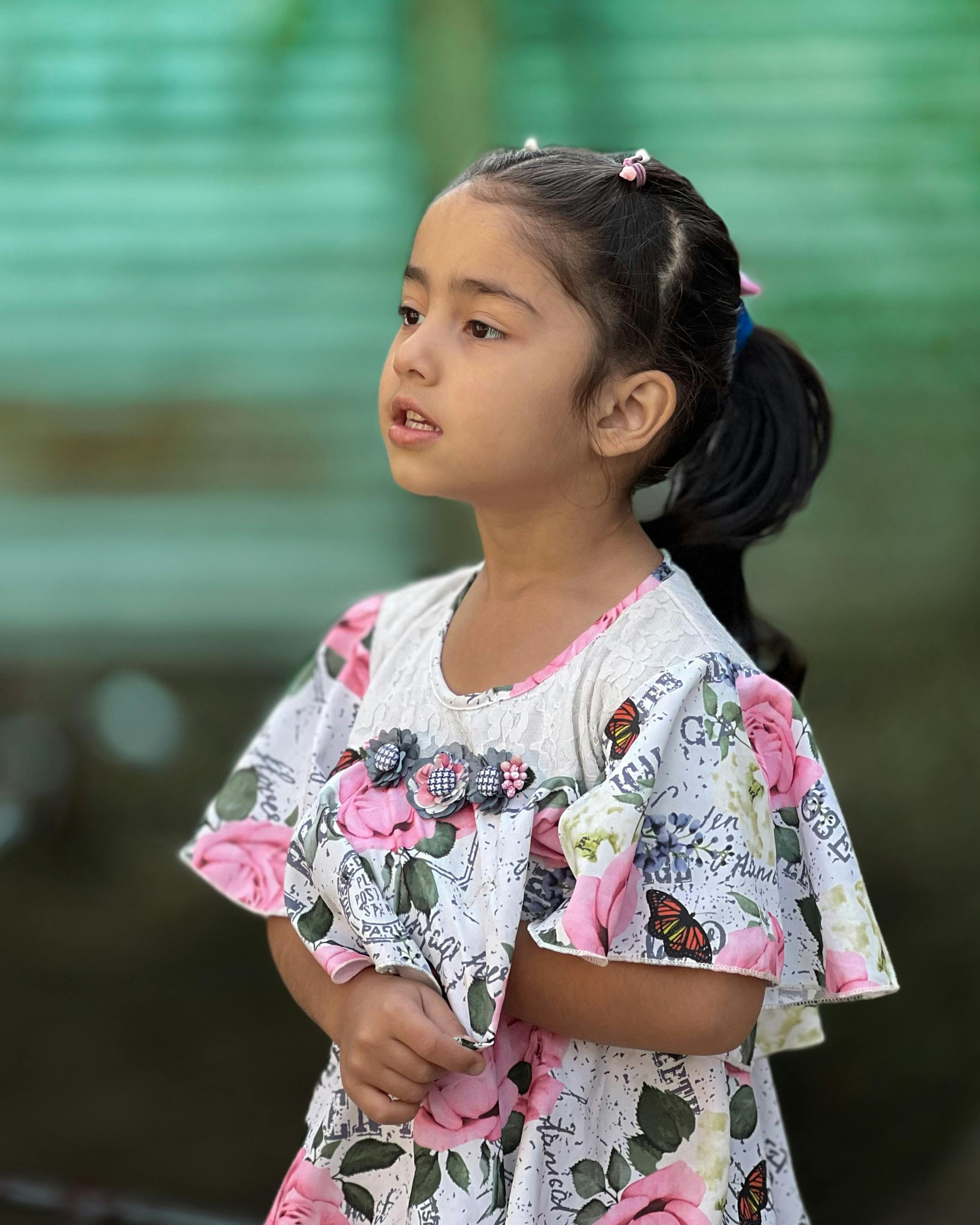 Free Portrait of a young girl wearing a colorful floral dress, captured outdoors. Stock Photo