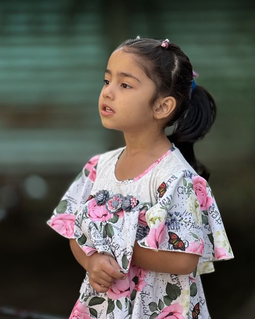 Free A young girl in a colorful floral dress stands outdoors, exuding innocence and charm. Stock Photo