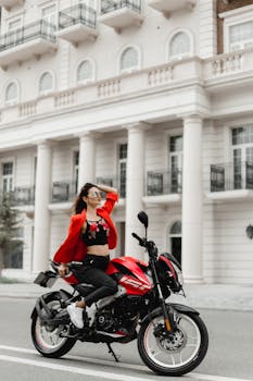 Fashionable woman posing on a red motorcycle in urban Baku street scene.