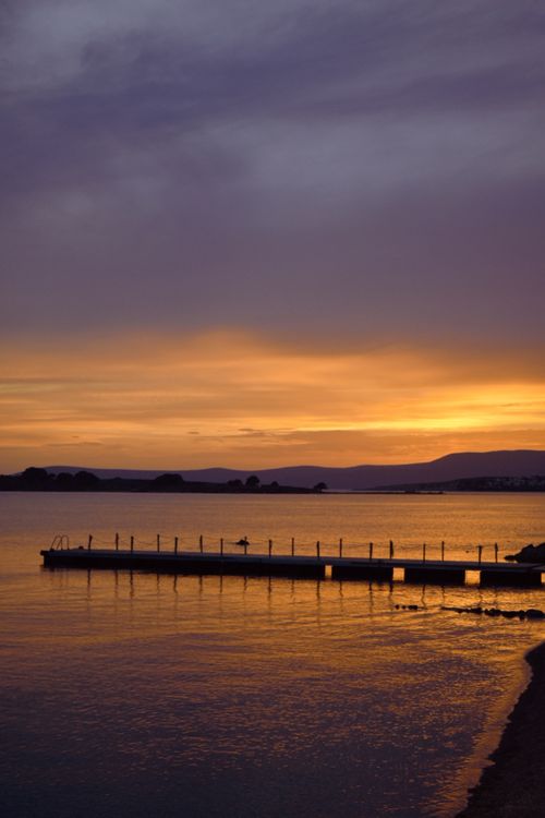 Free Captivating sunset over a serene lake with a silhouetted pier, perfect for tranquil landscapes and scenic beauty. Stock Photo