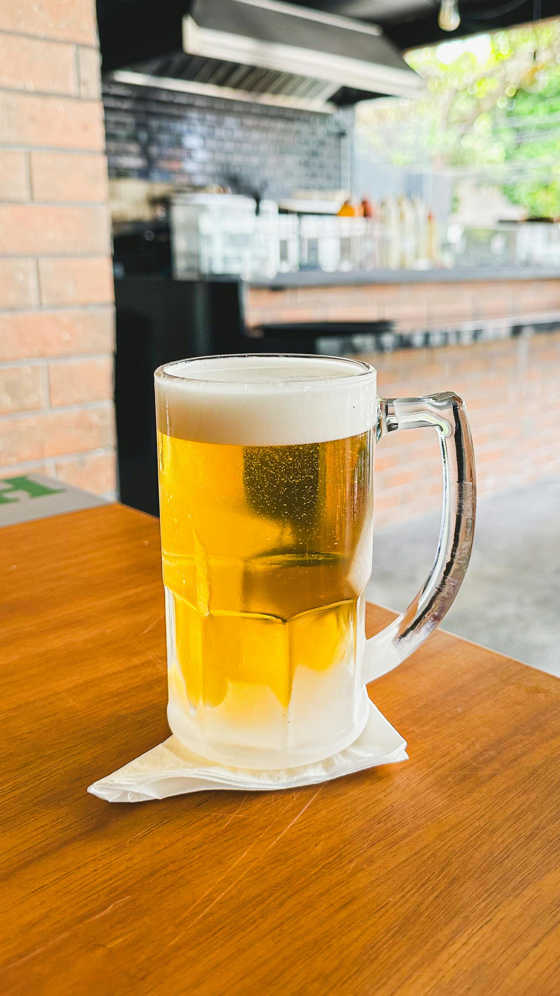 Chilled beer mug on wooden table in an outdoor restaurant setting. Refreshing and inviting.