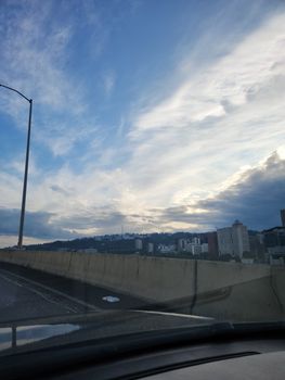 Capture of a city skyline at dusk with dramatic clouds and road in the foreground.