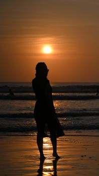 A serene scene of a woman's silhouette at sunset on a Bali beach.