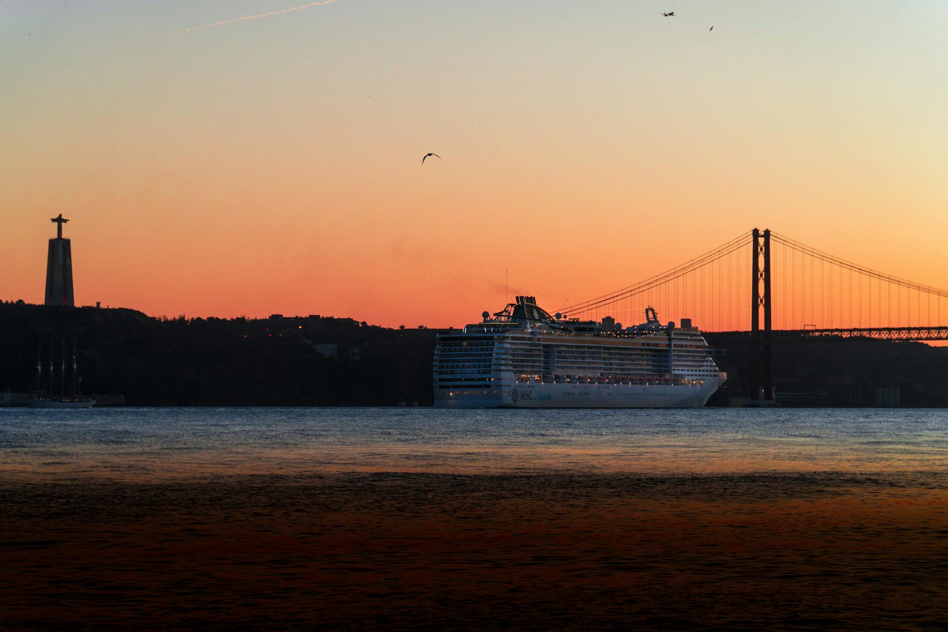Stunning view of a cruise ship passing under Lisbon's 25 de Abril Bridge at sunset.