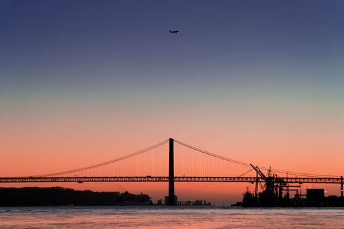 Free Beautiful sunset view over the 25 de Abril Bridge in Lisbon, Portugal, with a plane in the twilight sky. Stock Photo