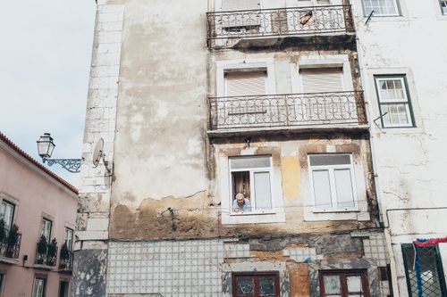 Free A rustic apartment building with a weathered facade and balconies. An adult leans out a window, adding life to the urban scene. Stock Photo