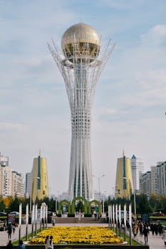Iconic Baiterek Tower in Astana, Kazakhstan, with urban skyline and floral foreground.