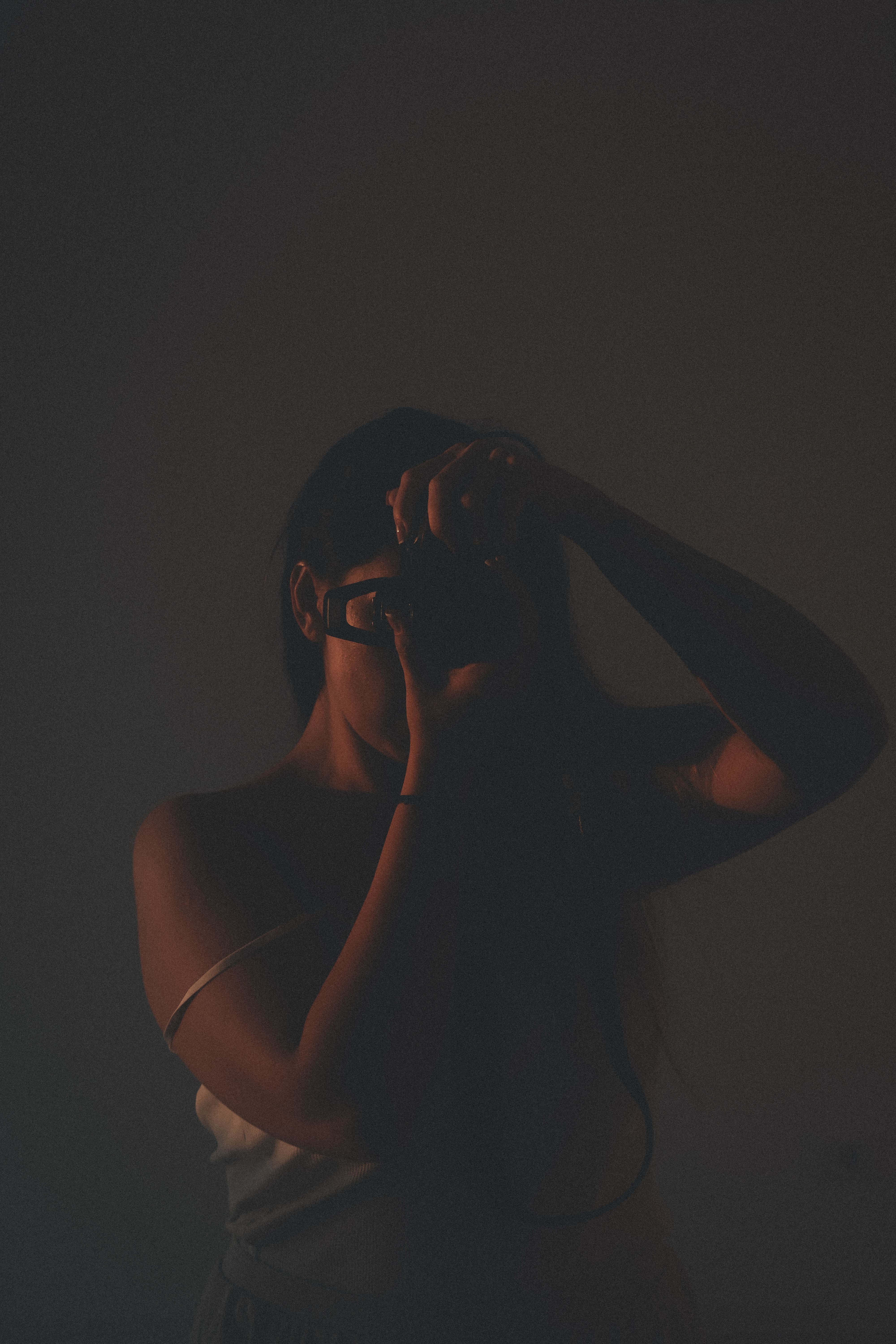 Artistic shot of a woman standing in darkness, taking a photo.