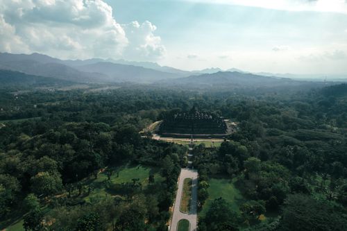 Free A breathtaking aerial shot of Borobudur Temple nestled in lush greenery under a bright sky. Stock Photo