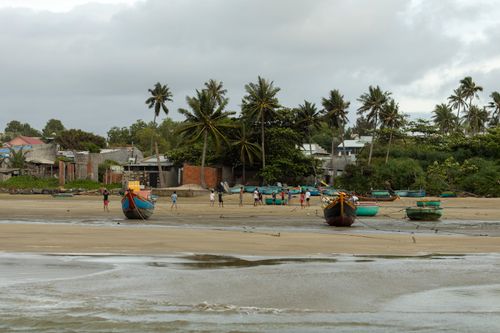 Free Fishing boats on a tropical beach with a village backdrop, capturing a serene seaside ambiance. Stock Photo