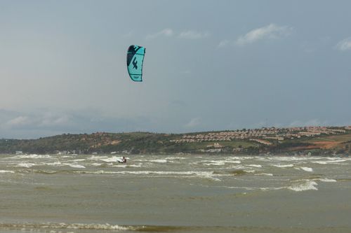 Free Kitesurfer riding waves on a windy coast with hilltop view. Perfect for adventure and nature enthusiasts. Stock Photo