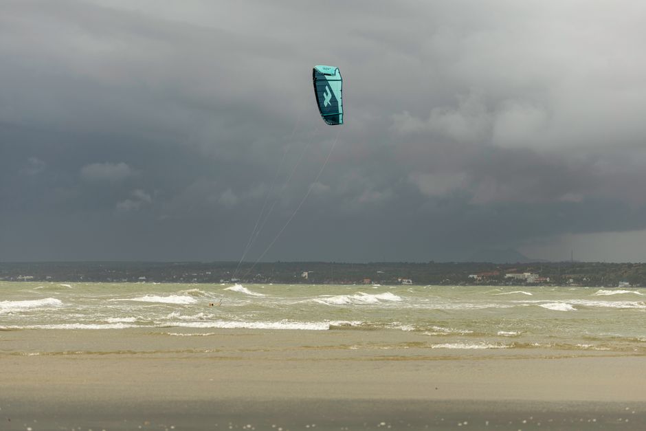 A kite surfer gliding across the sea under a cloudy sky, capturing the adventurous spirit of the ocean.