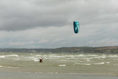 Free A kitesurfer skillfully maneuvers through choppy waves on a cloudy day at the beach. Stock Photo