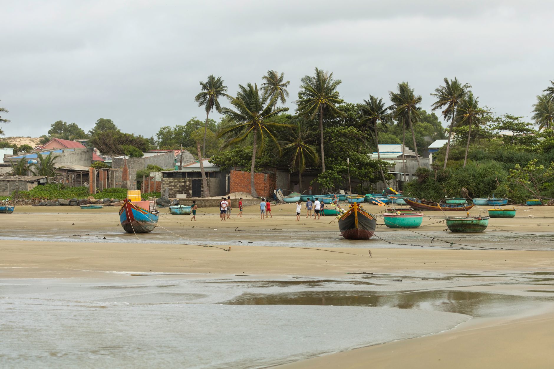 Scenic tropical beach with boats, palm trees, and a cloudy sky, offering an exotic coastal view.