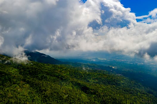 Dramatic aerial view of lush green mountains under a dynamic cloudscape in Banten, Indonesia.