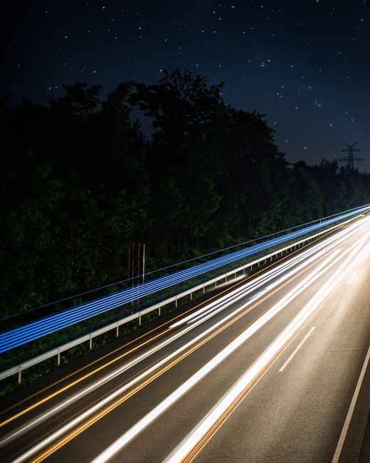 Dramatic long exposure photo of a highway under a starry night sky, showing light trails.