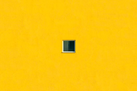 Bright yellow wall with a centered square window, showcasing minimalist architecture.
