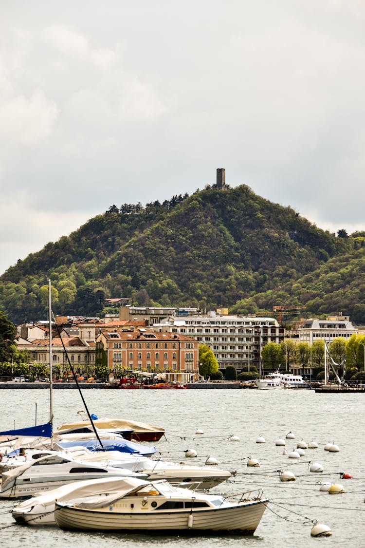 View Of Boats On The Shore Of Lake Como And Castello Baradello In The Background