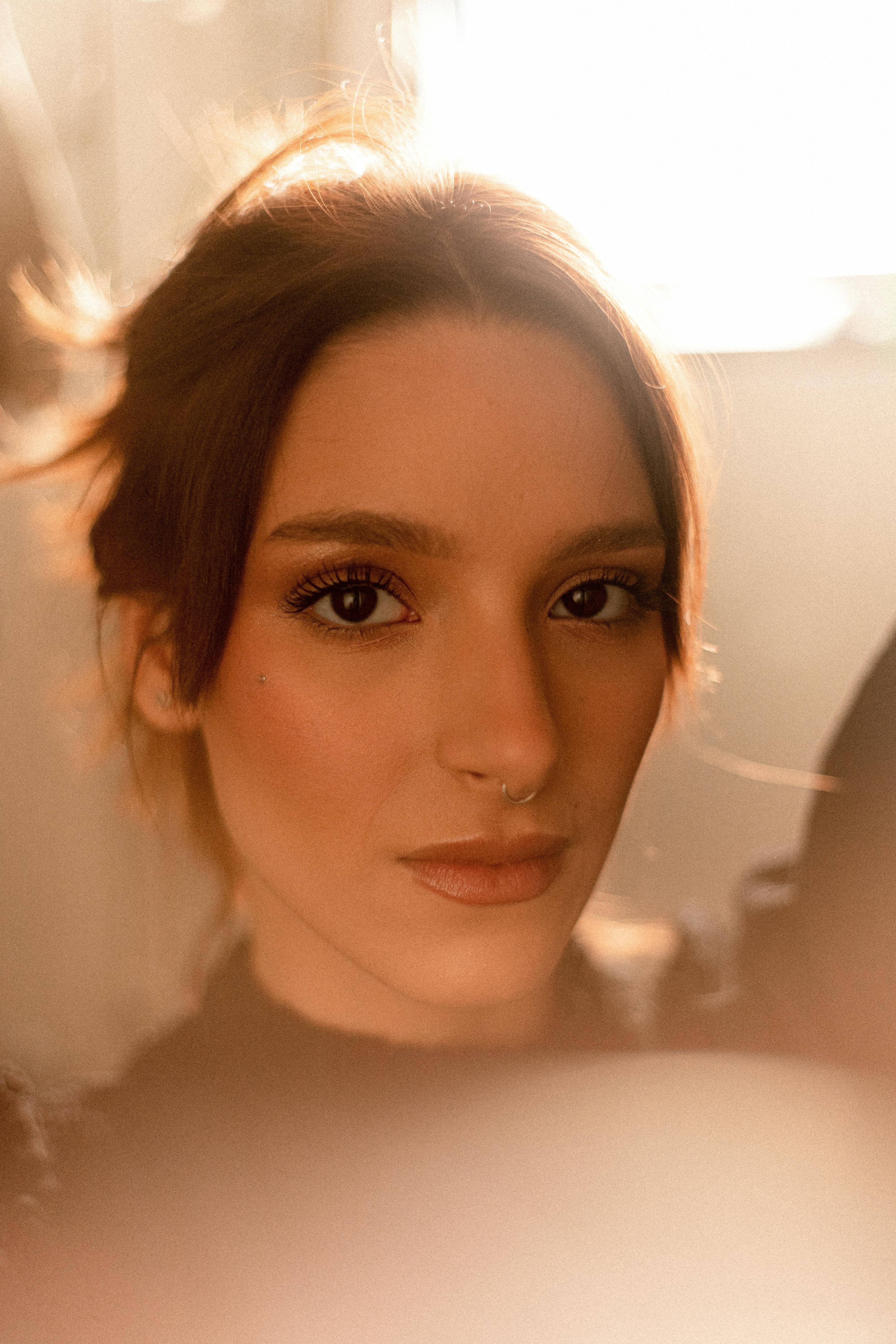 Close-up portrait of a woman with brown hair, soft lighting, and a nose piercing.