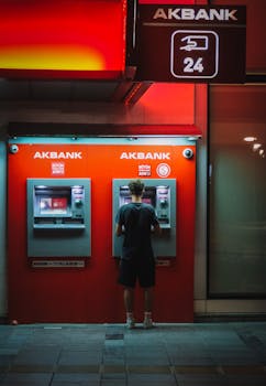 A person using an ATM at night in İzmir, Türkiye under red lighting.