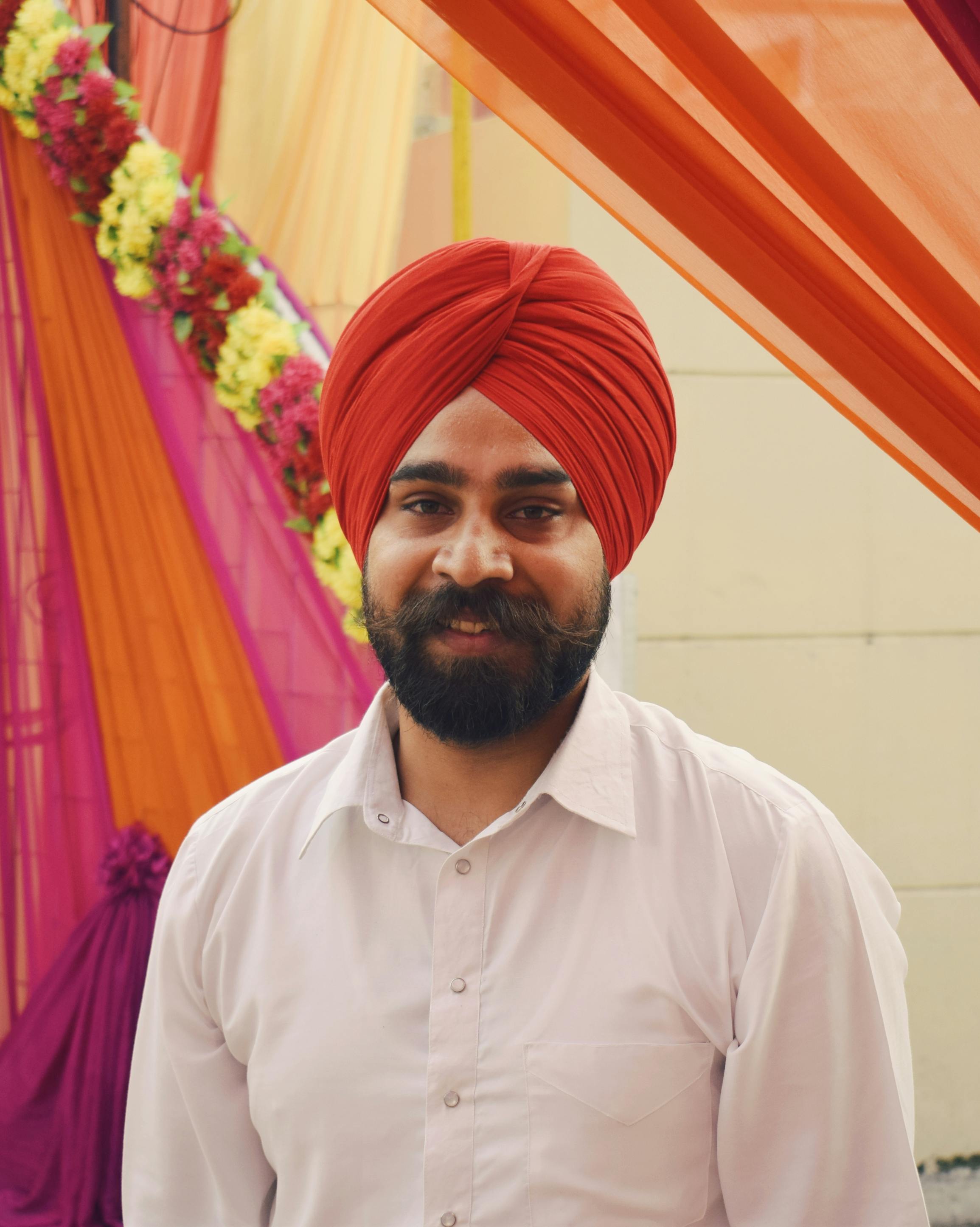 Portrait of a smiling Sikh man in a bright turban and white shirt, attending a festive event.