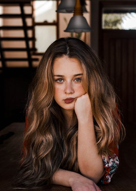 Portrait of a young woman resting her chin on her hand, showcasing long wavy hair and serious expression.