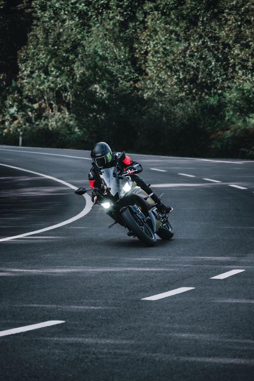 Free Dramatic scene of a motorcyclist racing on a curved road through dense forest. Stock Photo