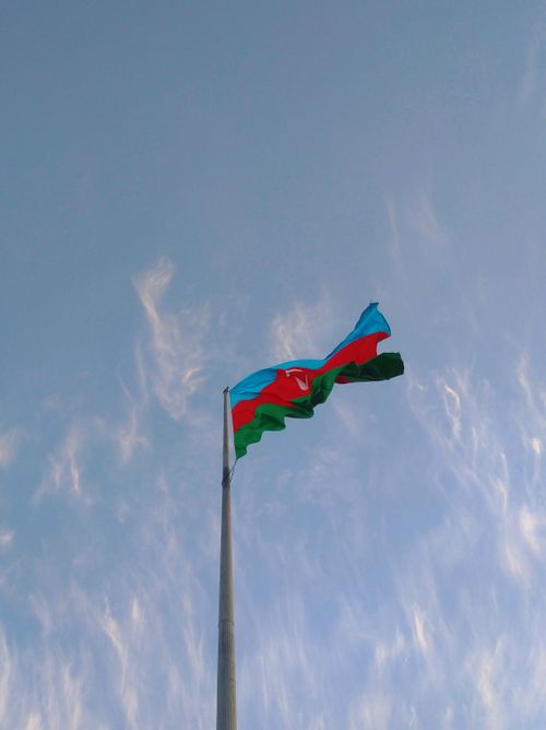 Free The national flag of Azerbaijan flying high against a serene blue sky, symbolizing national pride. Stock Photo