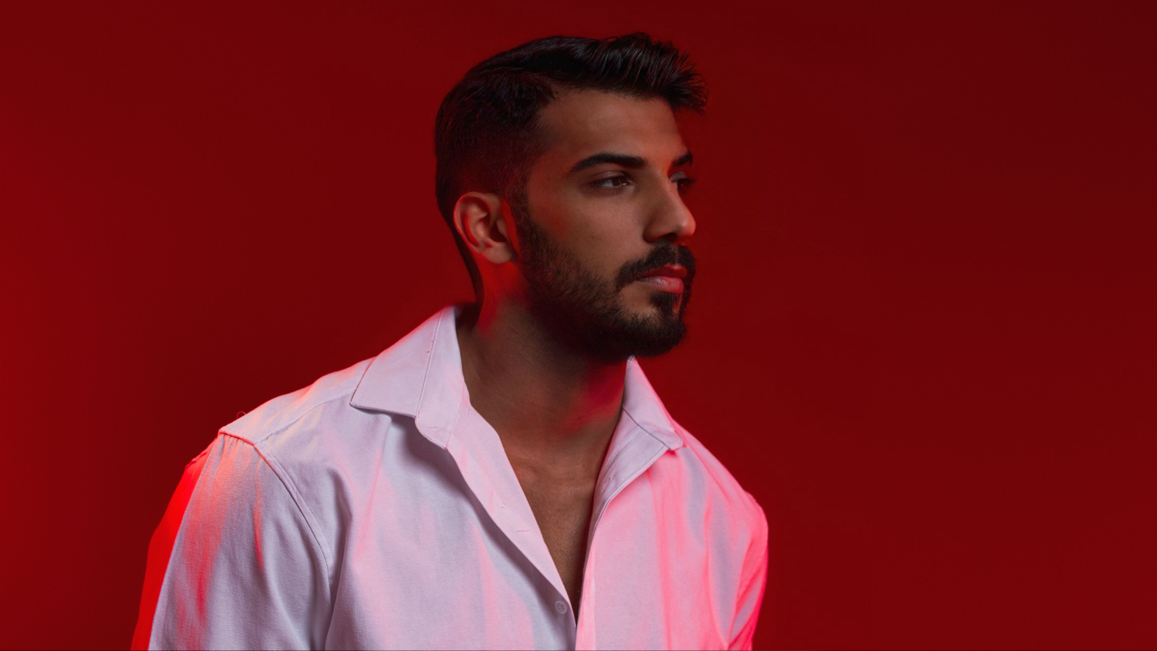 Portrait of a young man in a studio with a red background, highlighting modern fashion.
