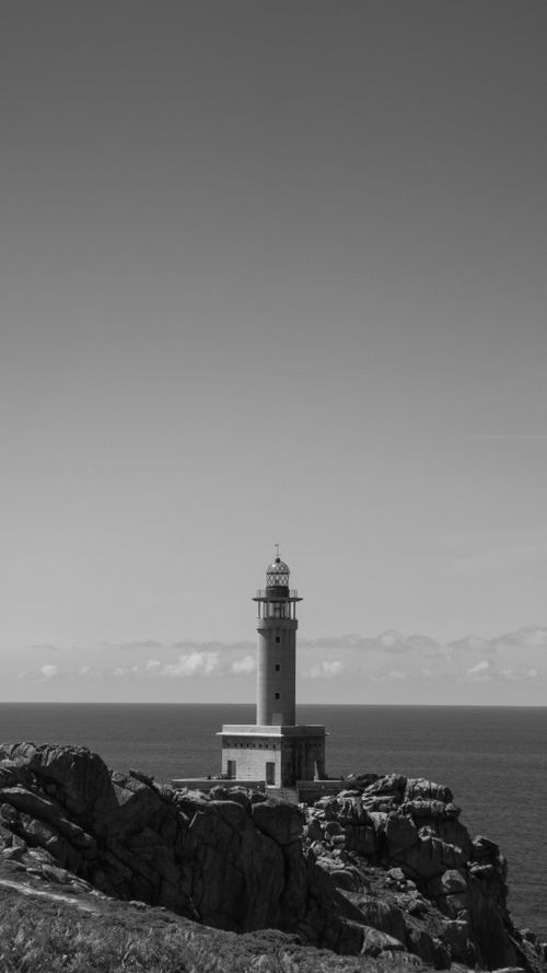Free Black and white photo of a lighthouse on a rocky seashore, sky background. Stock Photo