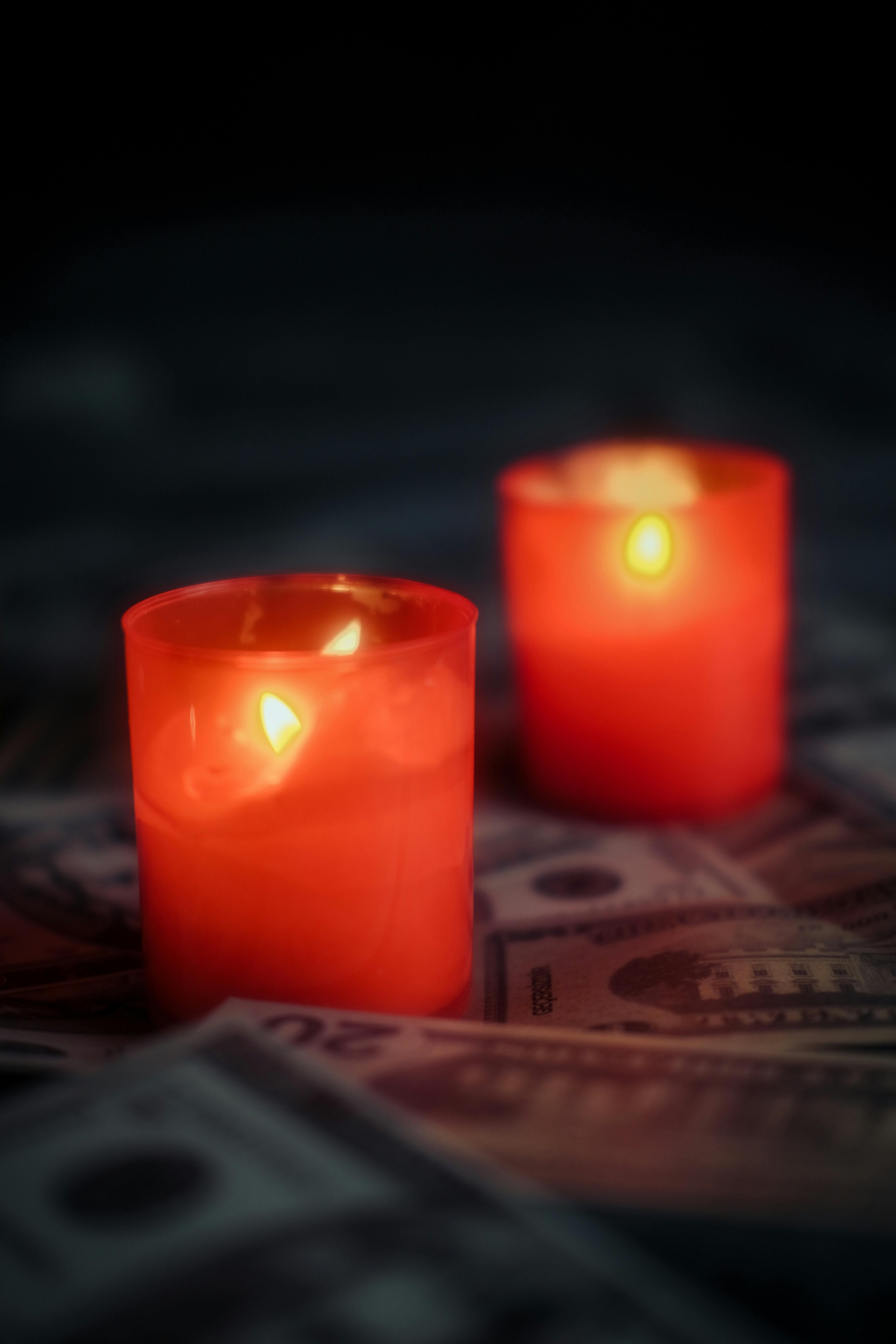 Two glowing red candles casting light on scattered US dollar banknotes.