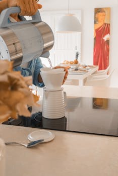 A person making pour over coffee in a bright, modern kitchen setting.