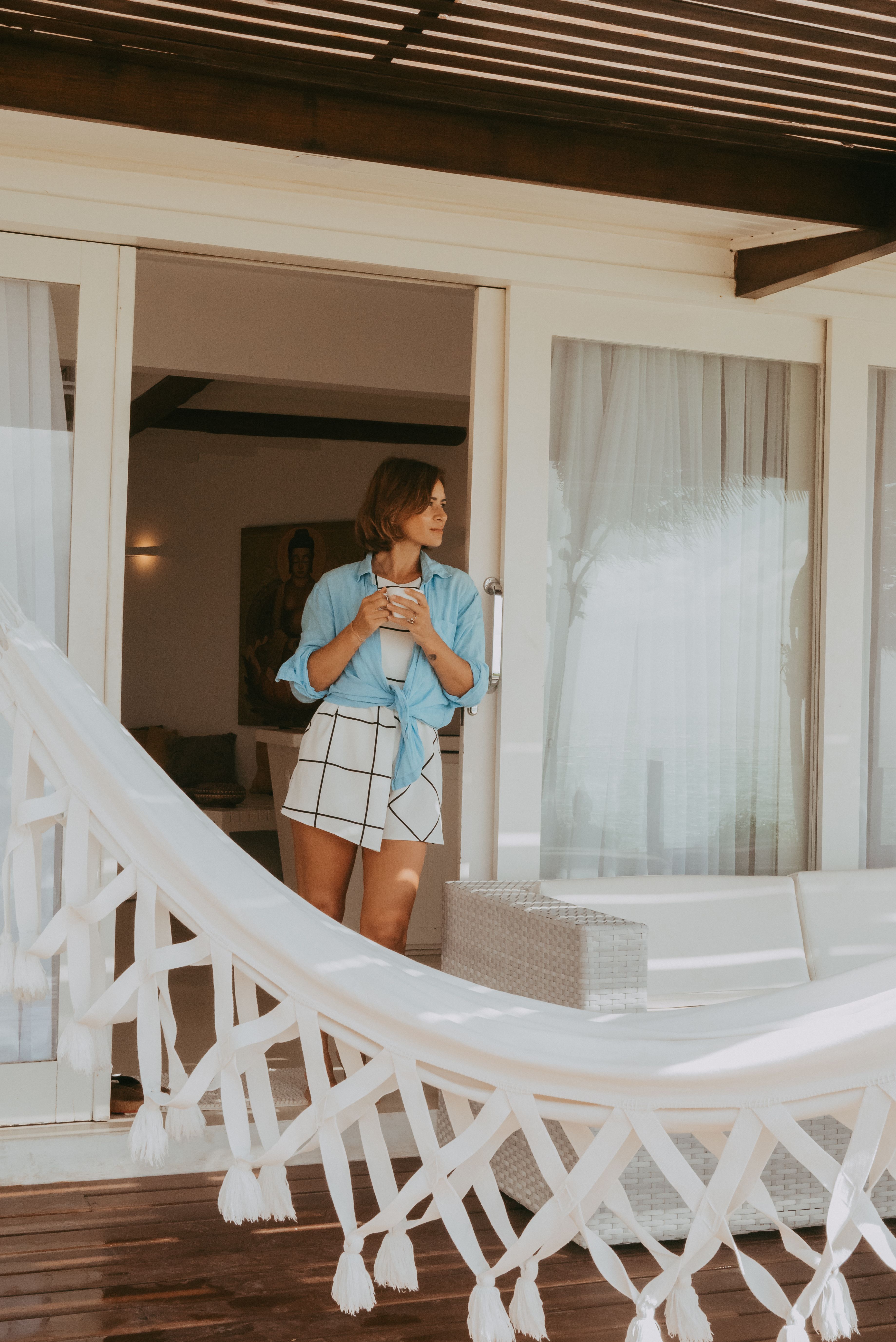 Woman in casual attire enjoying coffee by the window in a cozy room with natural light.
