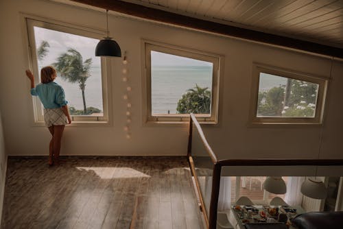 A woman standing in front of a window looking out at the ocean
