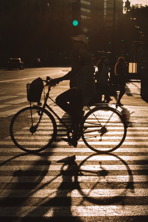 Free Silhouette of a cyclist at sunset crossing a city street in Valencia, Spain, highlighting urban life. Stock Photo