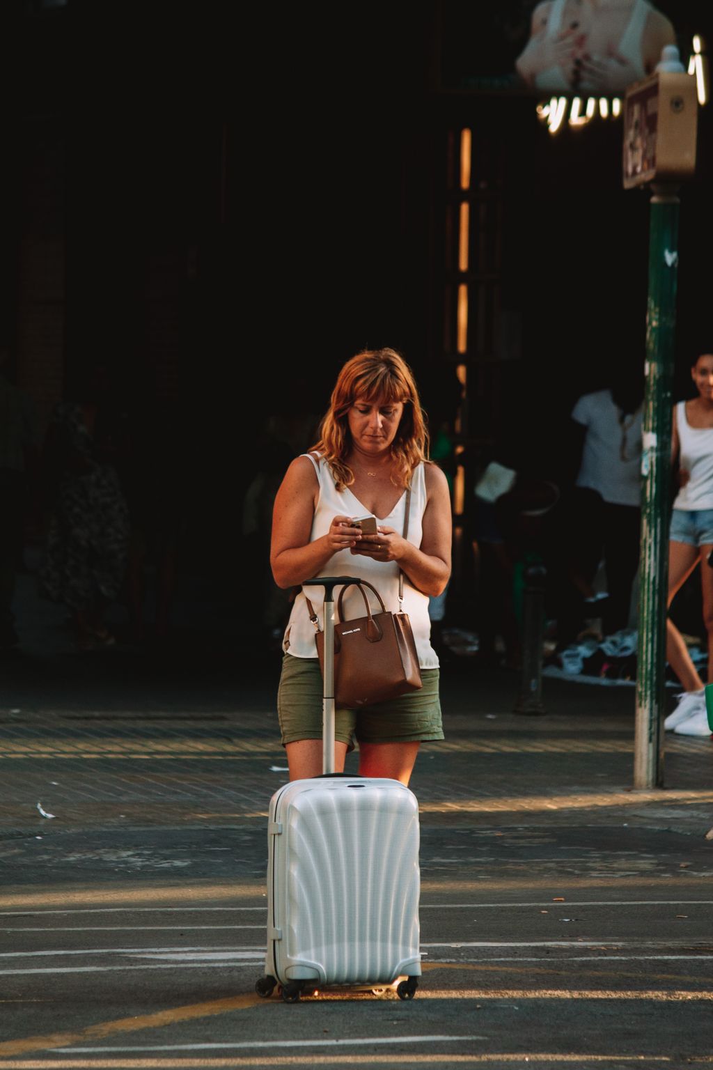 Someone messaging from a street abroad, suitcase beside them