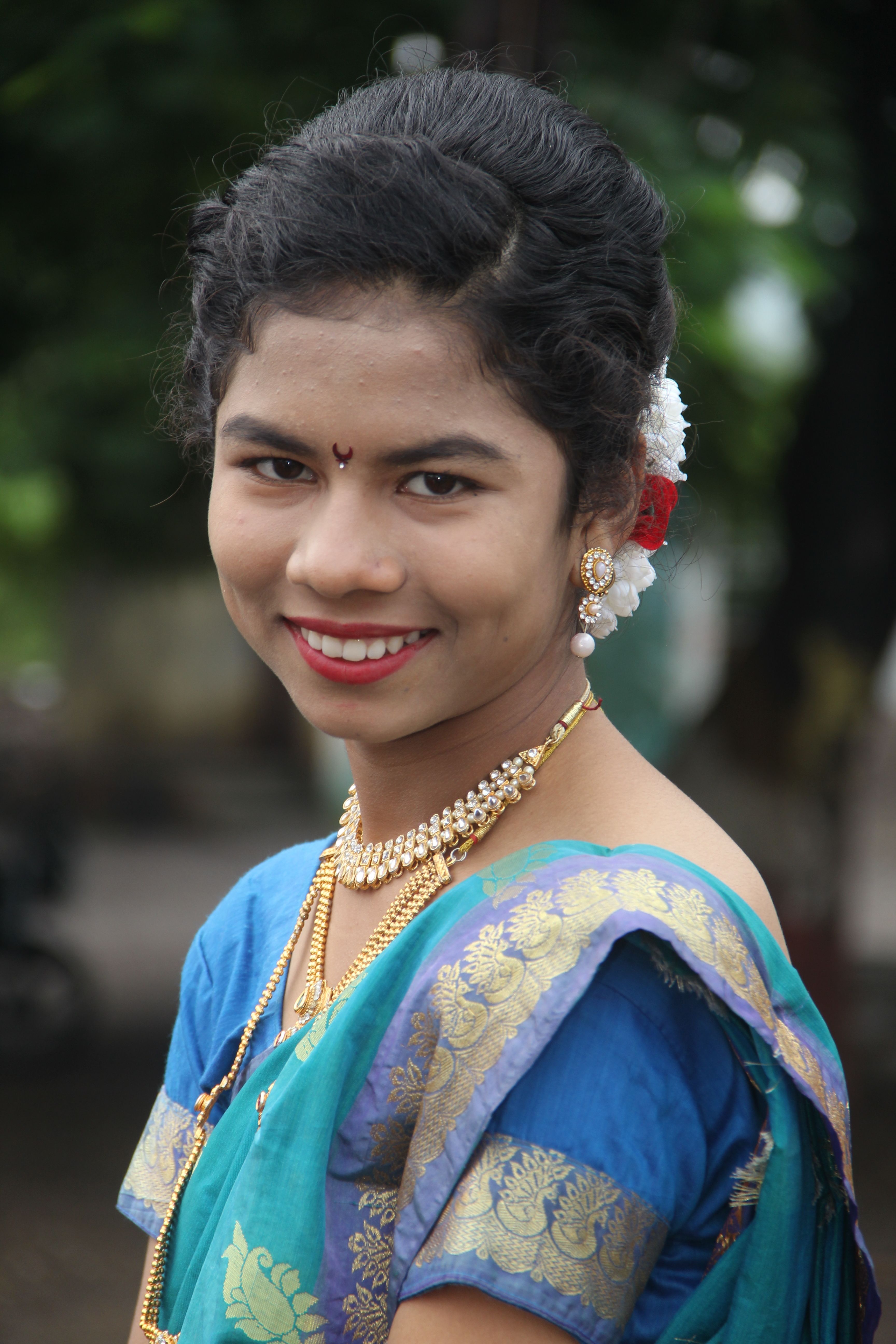 Young woman wearing traditional festive attire with jewelry and a smile, outdoors.