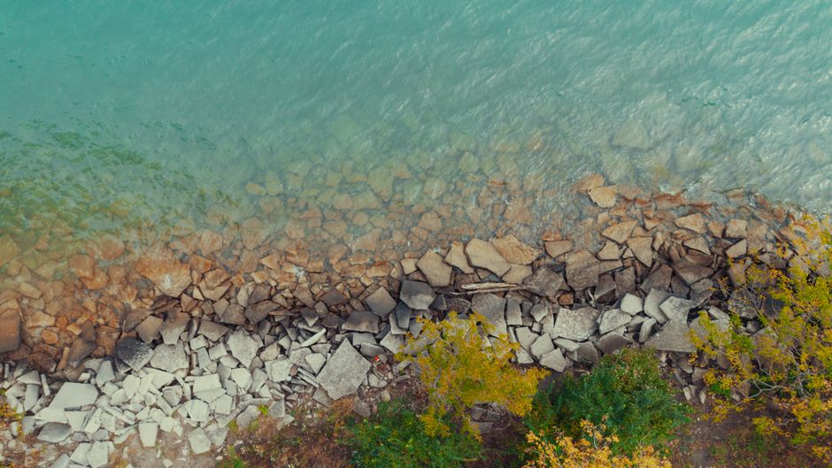 Spectacular Private 20 Minute River Ride Tour Review: Soaring Over Detroit's Iconic Waterway Review 2026 - Aerial view of a rocky shoreline meeting turquoise water, surrounded by greenery.