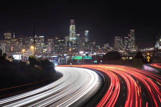 Stunning night view of San Francisco skyline with light trails from traffic on curving highway.