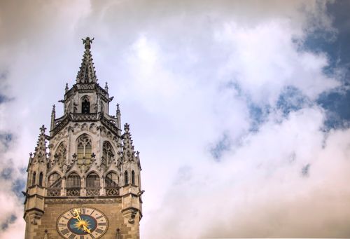 A majestic gothic clock tower in Munich with dramatic clouds in the background.