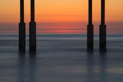 Tranquil scene of ocean waves under a pier with a vibrant sunset sky.