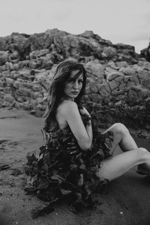 Free A black and white portrait of a woman wrapped in foliage on a rocky beach setting in Türkiye. Stock Photo