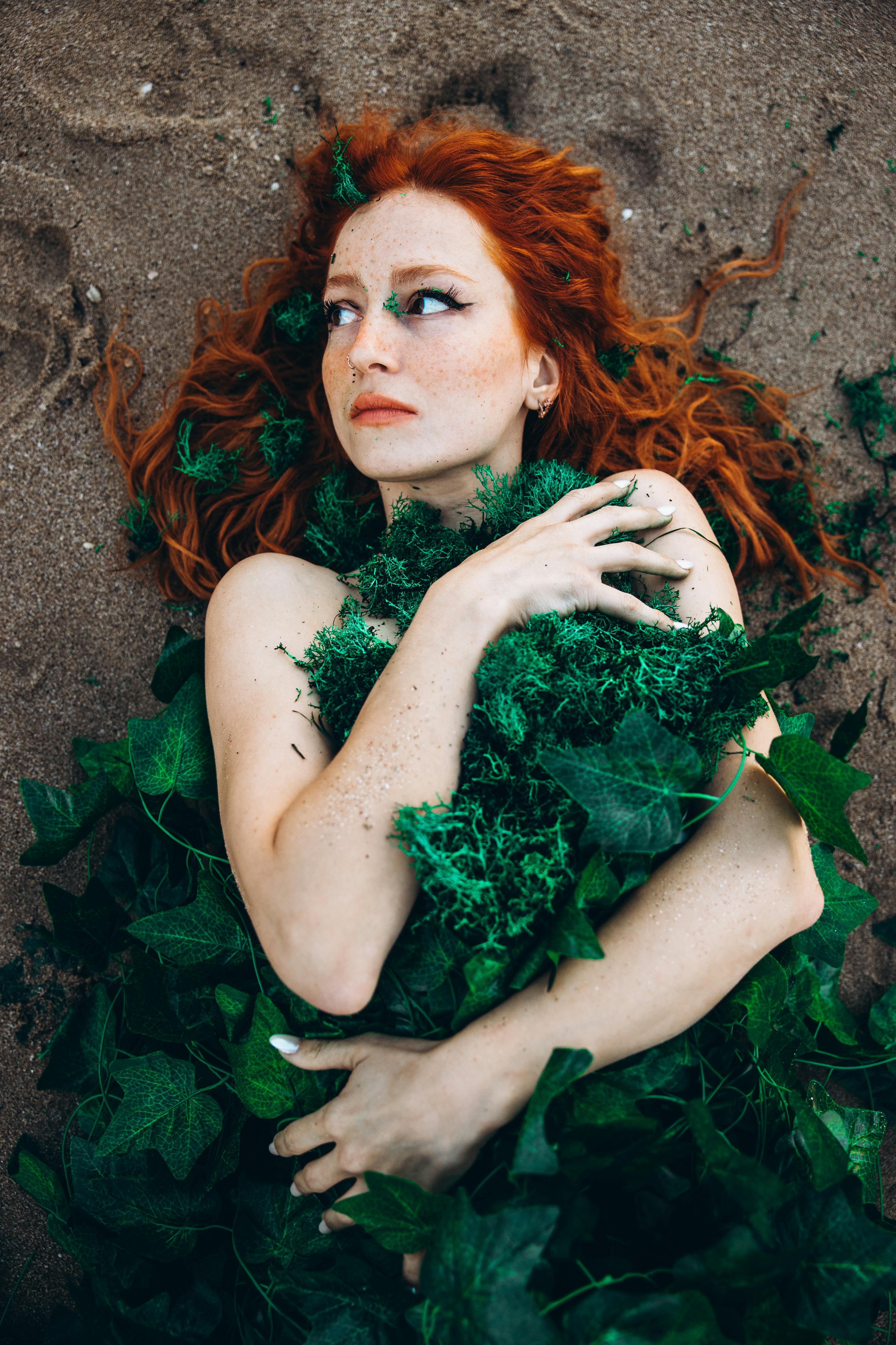 a woman with red hair and green leaves on her body