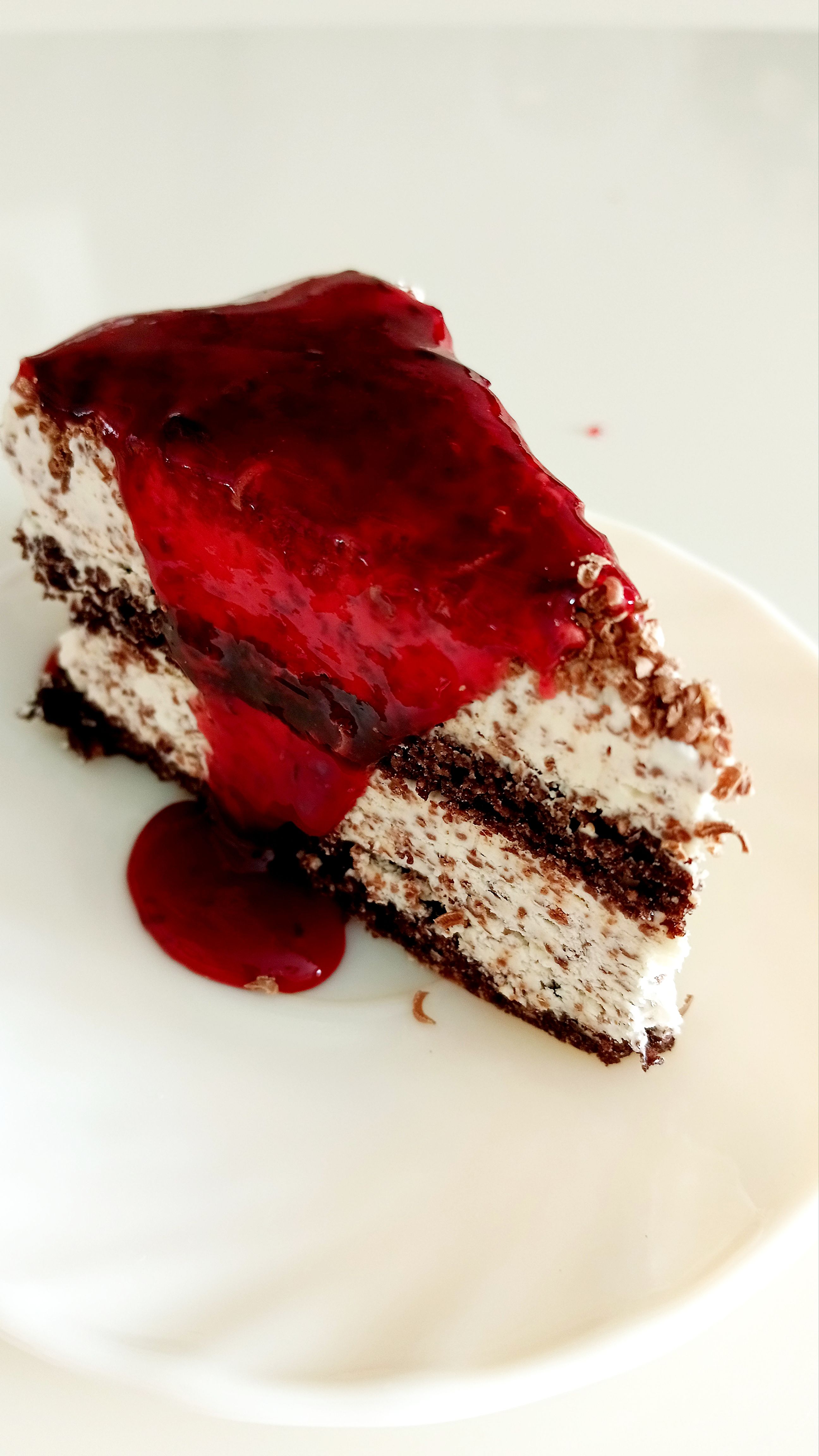 A mouthwatering slice of chocolate cake topped with a rich berry glaze on a white plate.