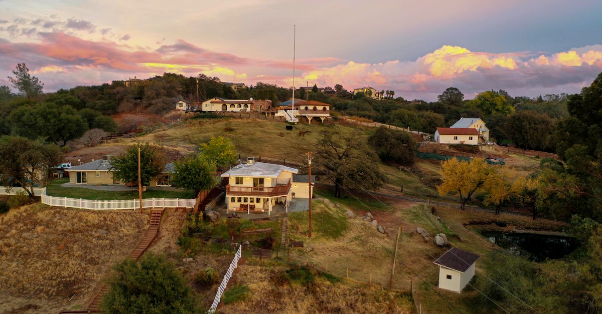 Aerial view capturing a serene hillside community with vibrant sunset skies, showcasing rural homes and autumn foliage.
