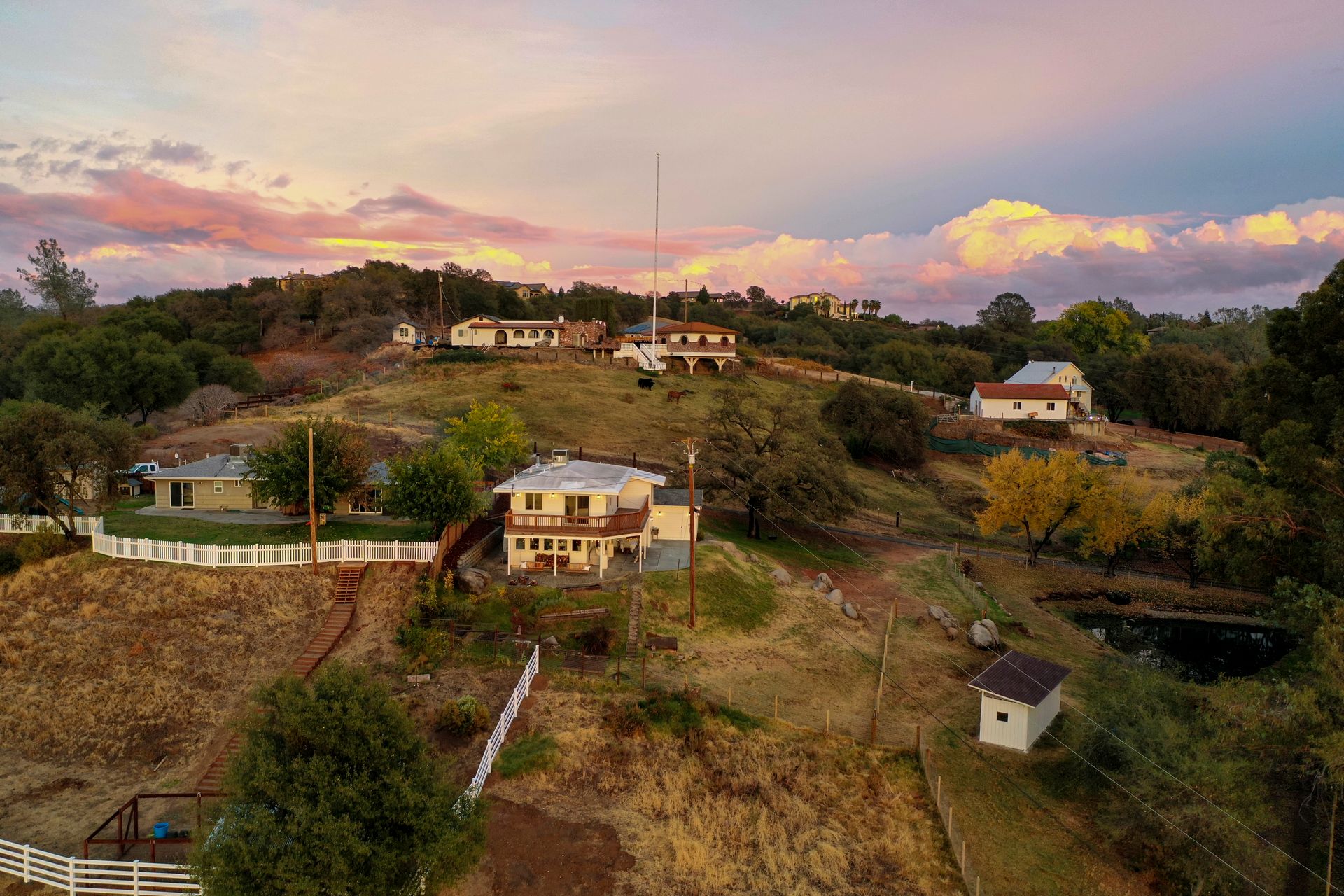 Aerial view capturing a serene hillside community with vibrant sunset skies, showcasing rural homes and autumn foliage.